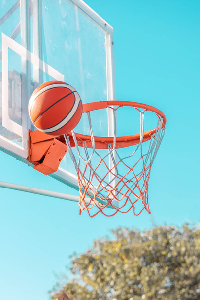 An orange basketball ball in hoop on a blue sky background. Side view. - Foto, afbeelding