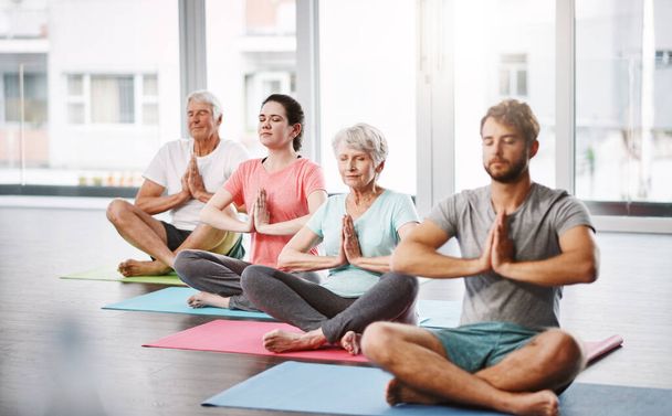 Full length shot of a group of people meditating while practicing yoga. - 写真・画像