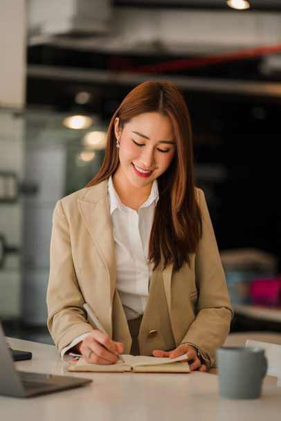 Очаровательная молодая азиатская бизнесвумен, работающая над своим проектом с ноутбуком за столом. вертикальная картинка - Фото, изображение