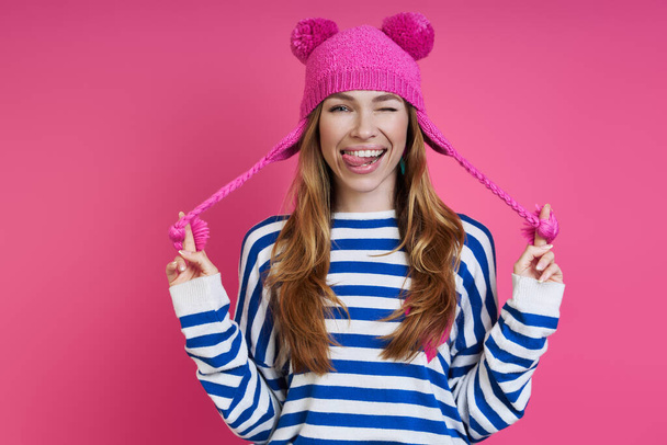 Playful young woman adjusting her pink hat while standing against colored background - Foto, imagen