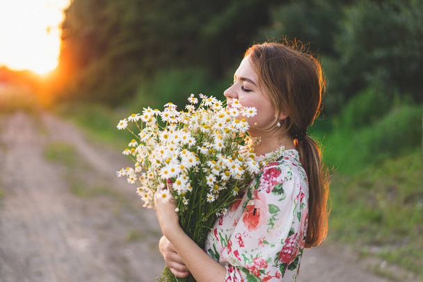 Portrait woman with chamomile flowers at sunset. Life without allergies, breathe freely. Woman having fun in summer on nature. Woman dreaming and smiling against the background of a camomile field. - 写真・画像
