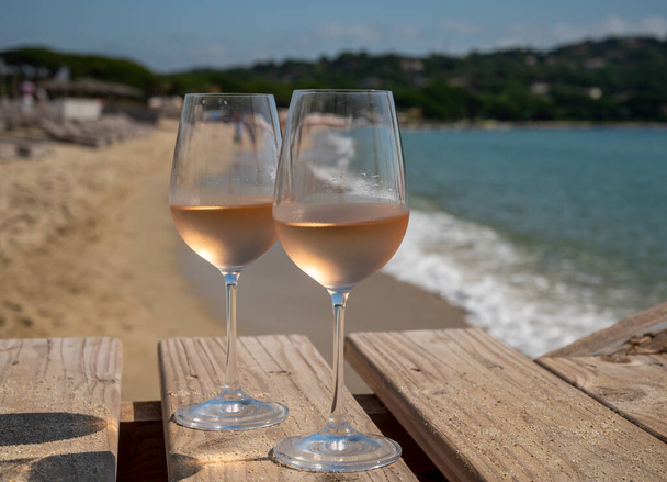 Gläser kalten Rosenweins aus der Provence serviert im Freien auf einem hölzernen Yachthafen mit Blick auf blaues Wasser und weißen Sandstrand Plage de Pampelonne in der Nähe von Saint-Tropez, Sommerurlaub in Frankreich - Foto, Bild