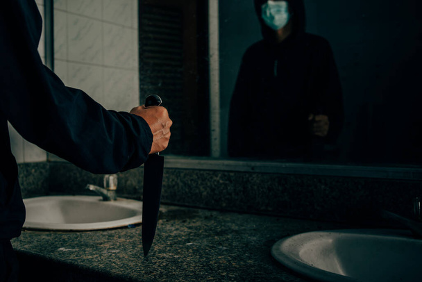 Visão traseira de um assassino segurando uma faca Na casa de banho, ele estava se olhando no espelho. - Foto, Imagem