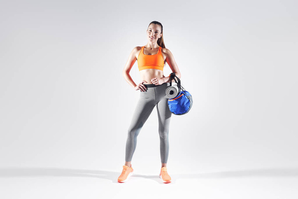 Full length of happy young woman in sports clothing carrying a bag against white background - Foto, immagini