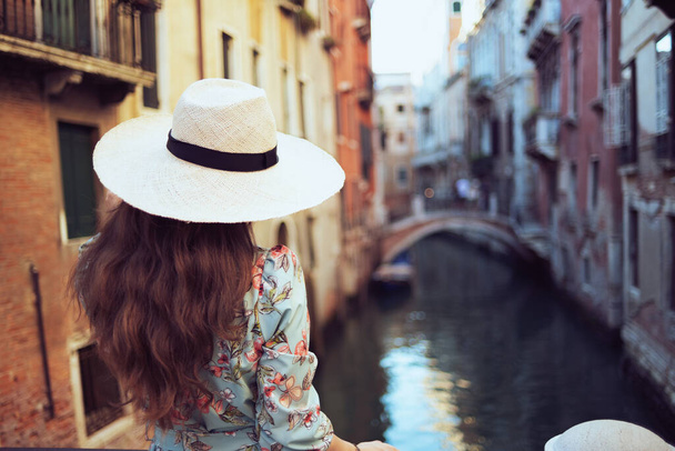 Seen from behind modern woman in floral dress with hat enjoying promenade in Venice, Italy. - Fotografie, Obrázek