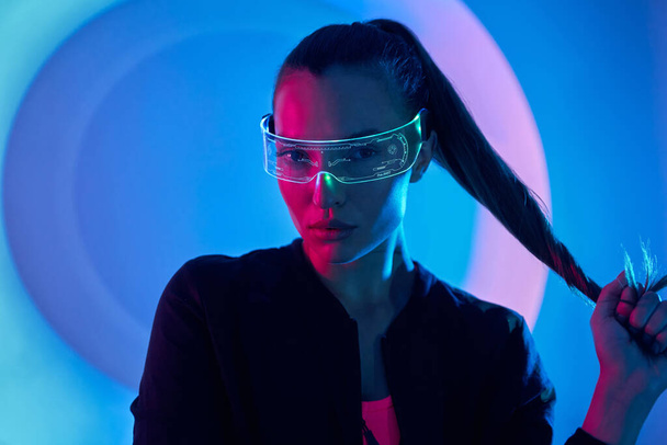 Confident young woman in futuristic glasses standing against colorful background - Photo, image