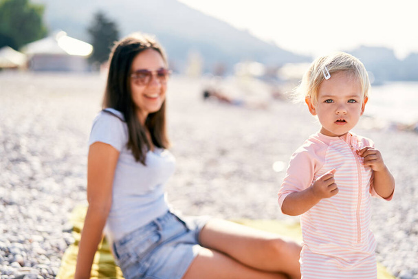 La bambina sta sulla spiaggia vicino alla mamma sorridente. Foto di alta qualità - Foto, immagini