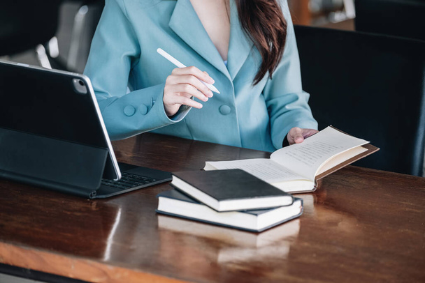 businesswoman showing a smiling face while reading a book developing financial and investing strategies and operating a computer tablet working on a wooden table - Fotografie, Obrázek
