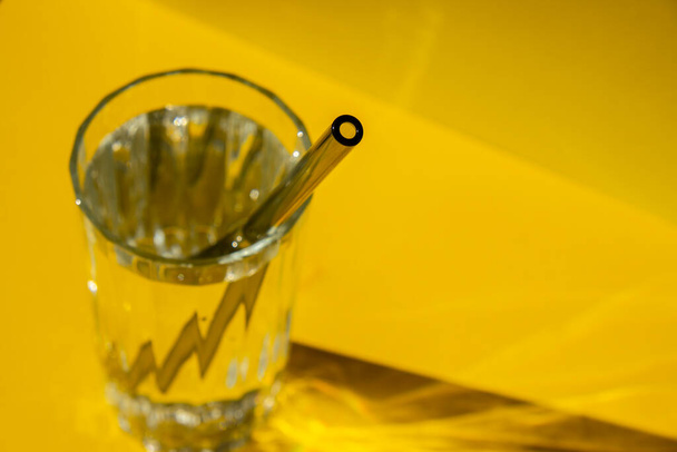 Pajitas de vidrio reutilizables en vidrio con agua sobre fondo amarillo Set de pajitas ecológicas para beber con cepillo de limpieza. Cero residuos, concepto libre de plástico. Estilo de vida sostenible. Residuos libres de vida Residuos bajos - Foto, imagen