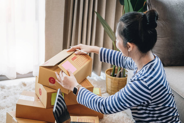 Онлайн мерчандайзинг бизнес-идея, красивая девушка упаковывает продукты в коробку доставки посылки, чтобы подготовить поставку клиенту в соответствии с заказом, полученным от клиента - Фото, изображение