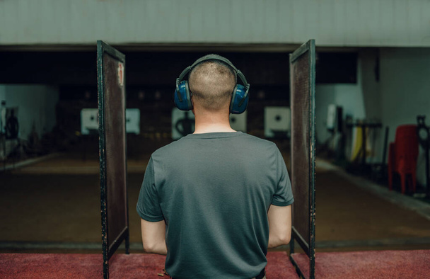 A professional man wearing earmuffs and goggles is practicing shooting a 9mm pistol inside a shooting range. - Foto, afbeelding