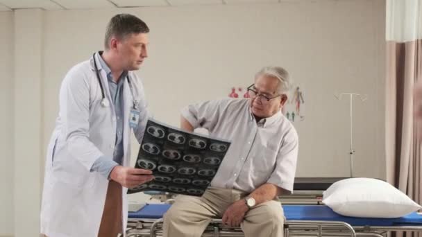 Kaukázusi férfi orvos egyenruhás egészségügyi ellenőrzések betegség idősebb beteg, diagnózis magyarázza röntgen film sürgősségi szobában ágy kórházi osztály, idős orvosi klinika, fájdalmas vizsgálati tanácsadó. - Felvétel, videó