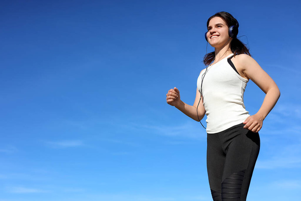 Young woman listening to music while running outdoors in morning, low angle view. Space for text - Fotoğraf, Görsel
