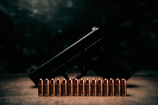 Ritratto di proiettili da 9 mm allineati su un vecchio pavimento di cemento con una pistola nella parte posteriore. - Foto, immagini