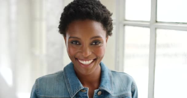 Closeup portrait and face of a young, happy woman smiling and laughing while standing alone. Headshot of a carefree and cheerful black female with an afro looking confident. A joyful lady by a window. - Filmmaterial, Video