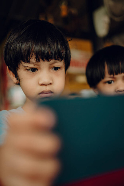 2 simpatici bambini asiatici seduti sul tavolo da pranzo con telefoni cellulari, concetto di dipendenza dal telefono Internet - Foto, immagini