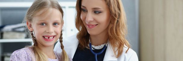 Portrait of smiling professional pediatrician posing with cute little girl on appointment. Doctor hold stethoscope tool for examining. Healthcare concept - Foto, Imagen