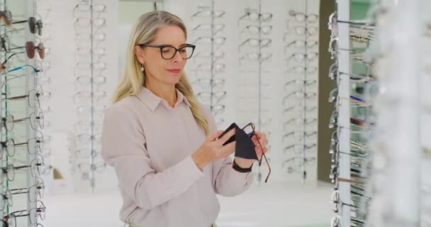 Mujer caucásica Optometrista limpiando gafas para la venta en su consultorio. Senior Optician limpiando y comprobando gafas en una tienda óptica antes de venderlas con espacio para copias. - Metraje, vídeo