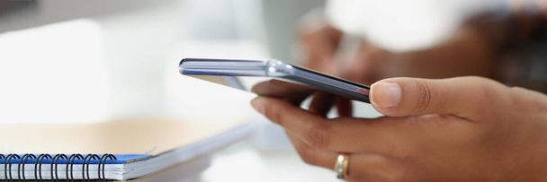 Close-up of woman using modern smartphone while sitting at table with spiral notebook in office. Write in diary and making call. Business, planning concept - Photo, Image