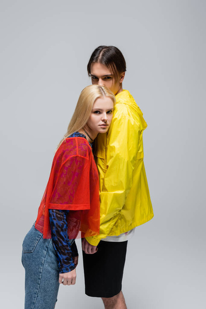 Fashionable couple in bright clothes looking at camera isolated on grey  - Zdjęcie, obraz