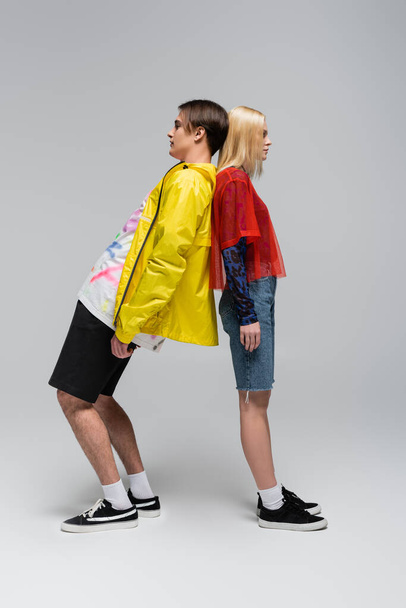 Side view of trendy couple standing back to back on grey background - Fotografie, Obrázek