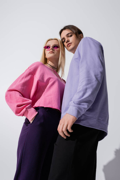 Low angle view of fashionable young couple posing on grey background - Zdjęcie, obraz