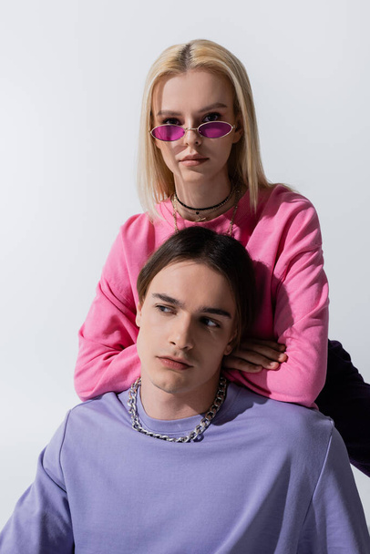 Young blonde model in pink sunglasses looking at camera near boyfriend isolated on grey  - Φωτογραφία, εικόνα