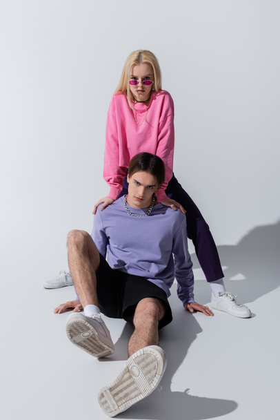 Young couple in sweatshirts and sneakers posing on grey background - Foto, Imagem