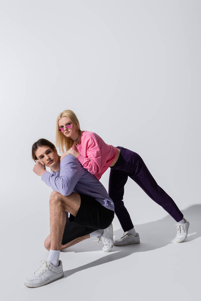 Stylish young couple in sneakers and sweatshirts posing on grey background - Zdjęcie, obraz