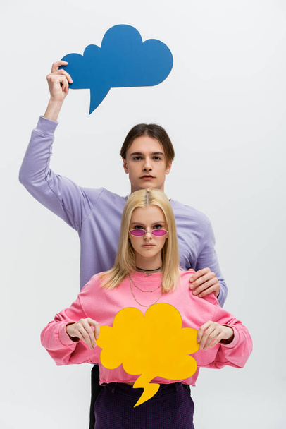 Stylish couple holding thought bubbles and looking at camera isolated on grey  - Foto, immagini