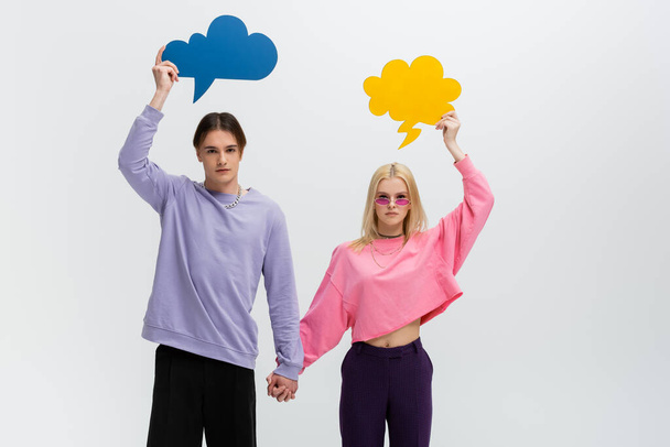 Stylish couple holding hands and thought bubbles isolated on grey  - Foto, Imagen