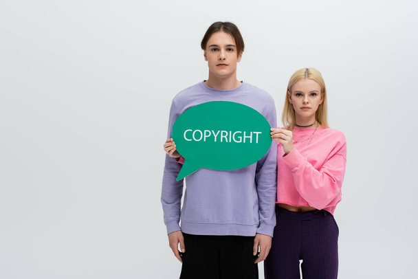 Young woman in sweatshirt holding speech bubble with copyright lettering isolated on grey  - Photo, image