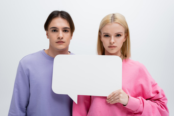 Young couple in sweatshirts holding white speech bubble isolated on grey  - Fotografie, Obrázek