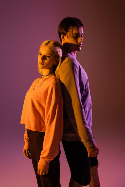 Young couple standing back to back on purple background with lighting  - Foto, immagini