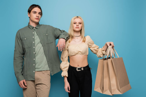 Young woman holding shopping bags near stylish boyfriend on blue background  - 写真・画像