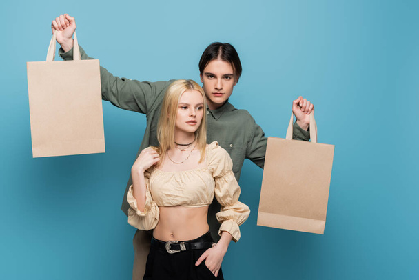 Stylish man holding shopping bags near girlfriend on blue background  - Valokuva, kuva