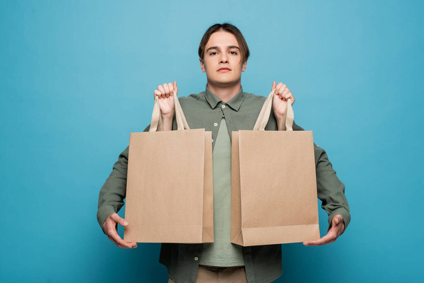 Mujer sosteniendo bolsas de compras cerca de novio con estilo sobre fondo azul  - Foto, Imagen