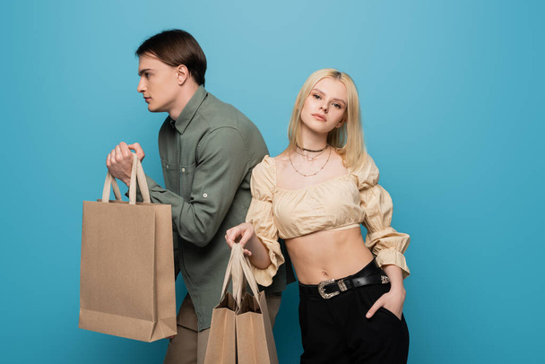 Young woman in blouse posing with shopping bags near boyfriend on blue background  - Fotoğraf, Görsel