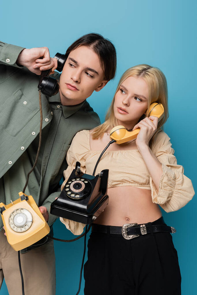 Fashionable couple talking on telephones and looking away on blue background  - Foto, Bild