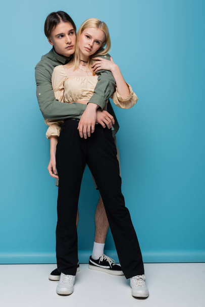 Full length of young man embracing stylish girlfriend on blue background  - Foto, Bild