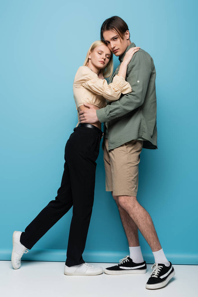 Stylish man in shirt hugging blonde girlfriend on blue background  - Foto, afbeelding