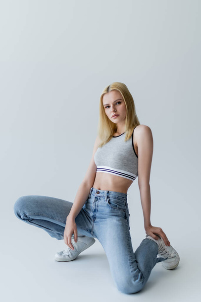 Trendy young woman in top and jeans posing on grey background  - Photo, Image