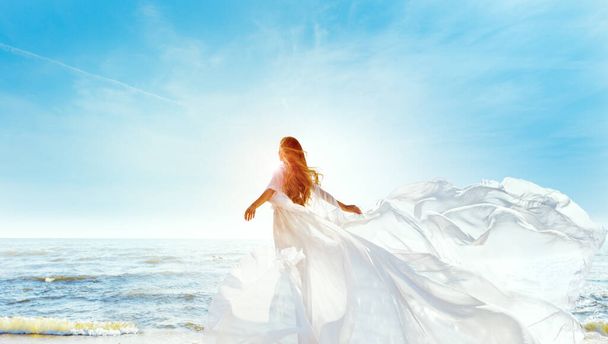 Model in White Dress Flying on Wind. Happy Woman Enjoying Sun looking away at Blue Sky. Carefree Girl dreaming at Sea Beach Resort. Freedom and Spiritual Relax Concept - Zdjęcie, obraz