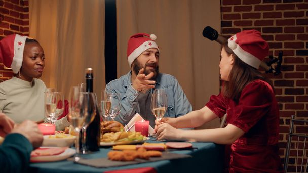 Festive people talking at Christmas dinner while enjoying traditional home cooked food. Joyful family members discussing at home while celebrating winter holiday together. - 写真・画像