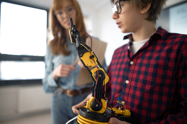 A college student presenting his builded robotic toy to young science teacher at robotics classroom at school. - 写真・画像