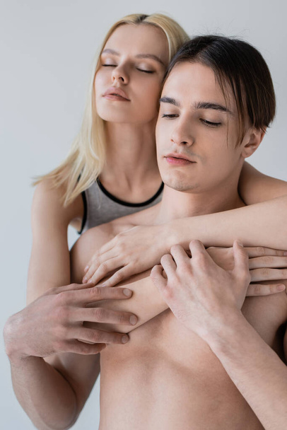 Portrait of woman embracing shirtless boyfriend isolated on grey  - Фото, изображение