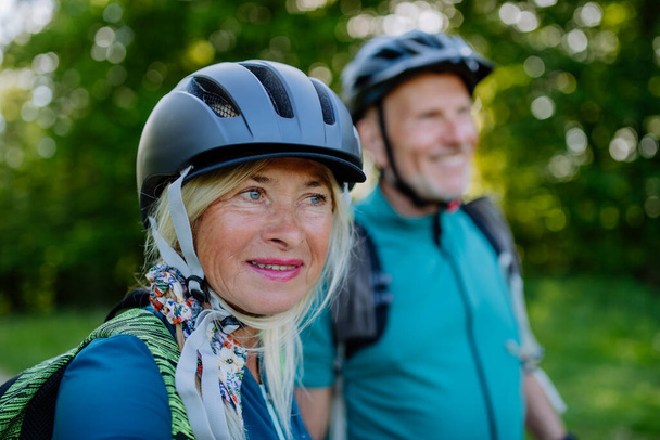 An active senior couple riding bicycles at summer park, woman with bicycle helmet, healthy lifestyle concept. - Foto, Bild