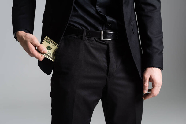 bijgesneden beeld van de mens in zwart pak met geld in de buurt zak geïsoleerd op grijs - Foto, afbeelding