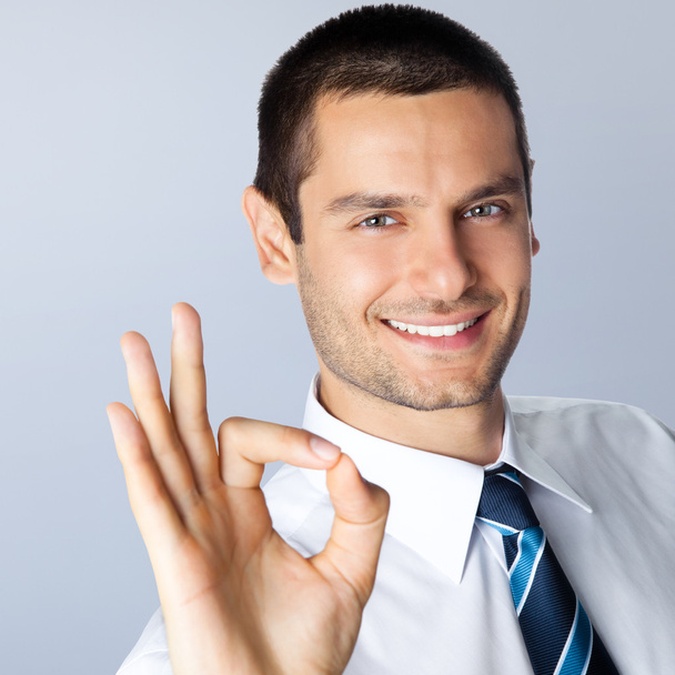 Businessman with okay gesture, against grey - Фото, изображение