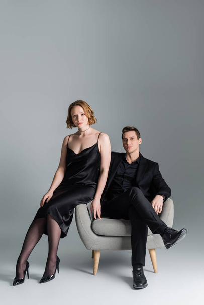 full length of confident man and woman posing near armchair on grey background - Fotografie, Obrázek